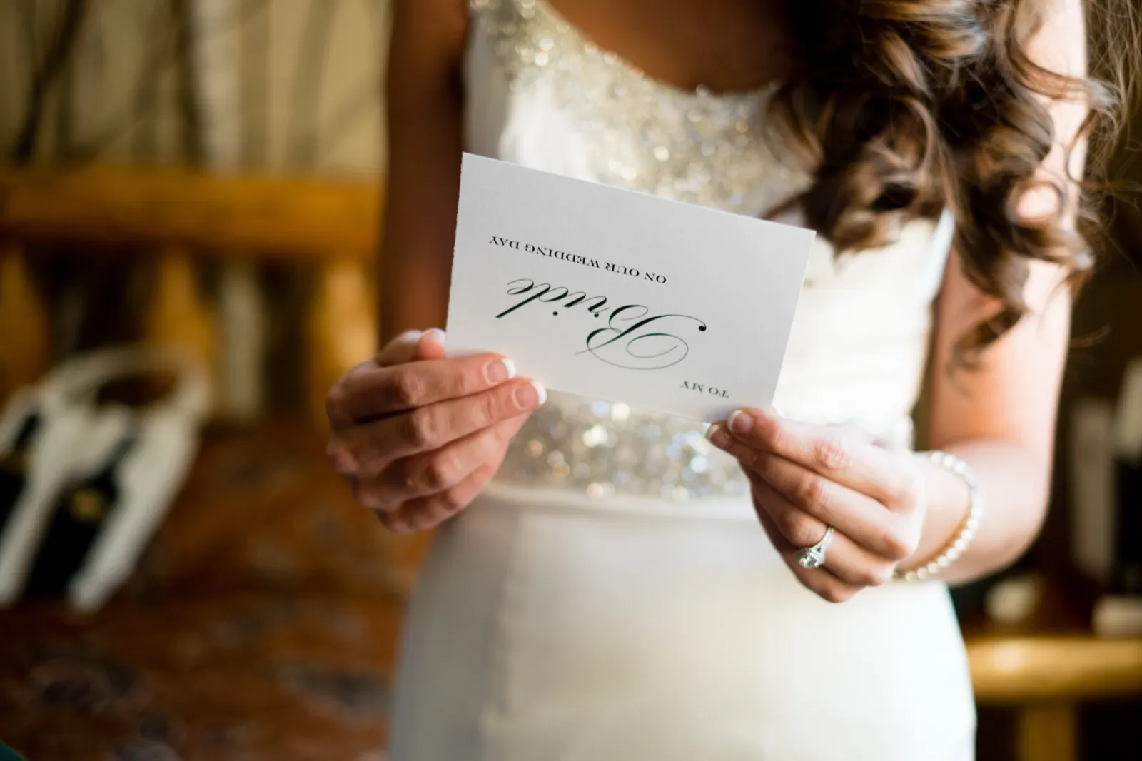 The bride holds a card reading 'To My Bride On Our Wedding Day' in front of her sequined gown, engagement ring and pearl bracelet visible on her hands. — Tim Larsen Photography, Brainerd Lakes MN
