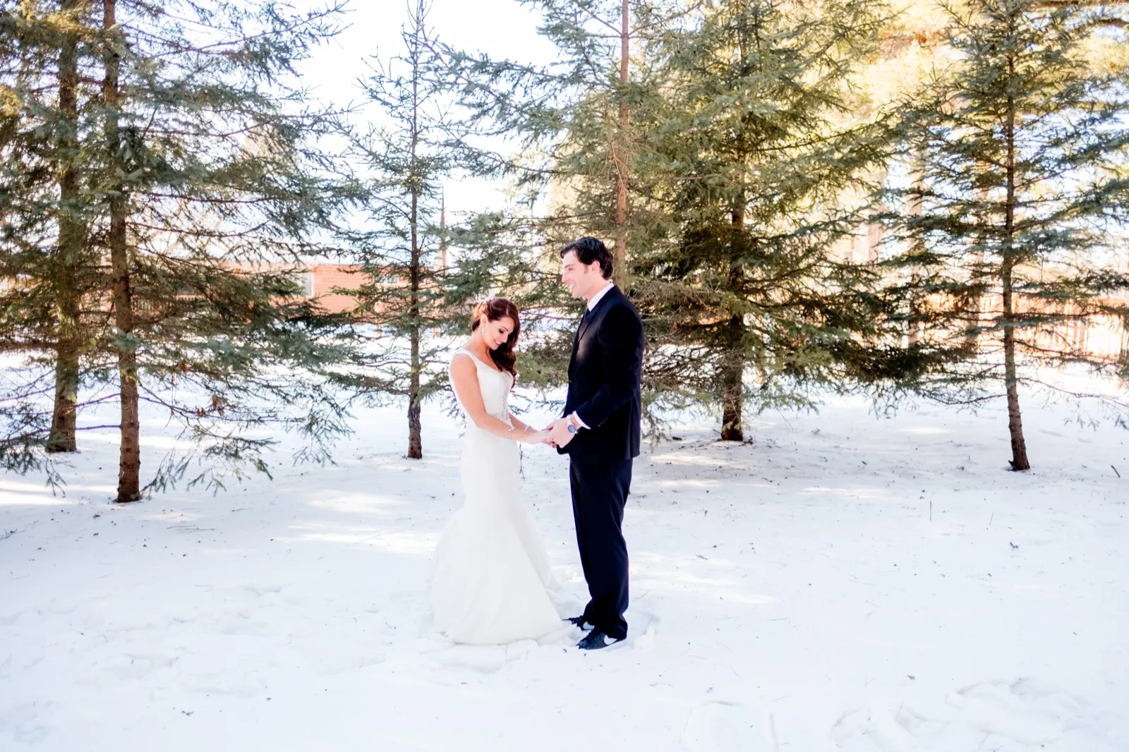 The bride and groom hold hands together among tall pine trees in deep snow on a sunlit winter afternoon. — Tim Larsen Photography, Brainerd Lakes MN