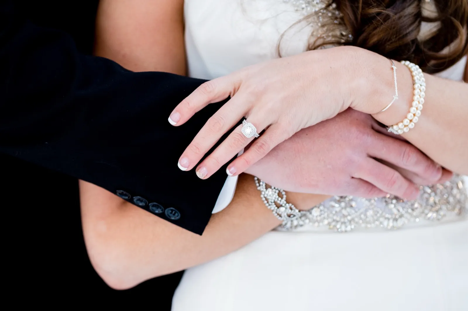 A close-up of the bride's hand resting on the groom's sleeve, showing her engagement ring, pearl bracelet, and the beaded detail of her gown. — Tim Larsen Photography, Brainerd Lakes MN