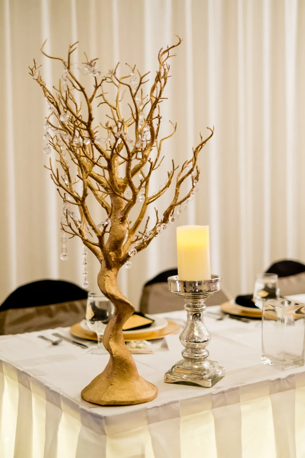 A tall gold-painted manzanita branch centerpiece with hanging crystals stands beside a lit pillar candle on a mercury glass holder at the head table. — Tim Larsen Photography, Brainerd Lakes MN