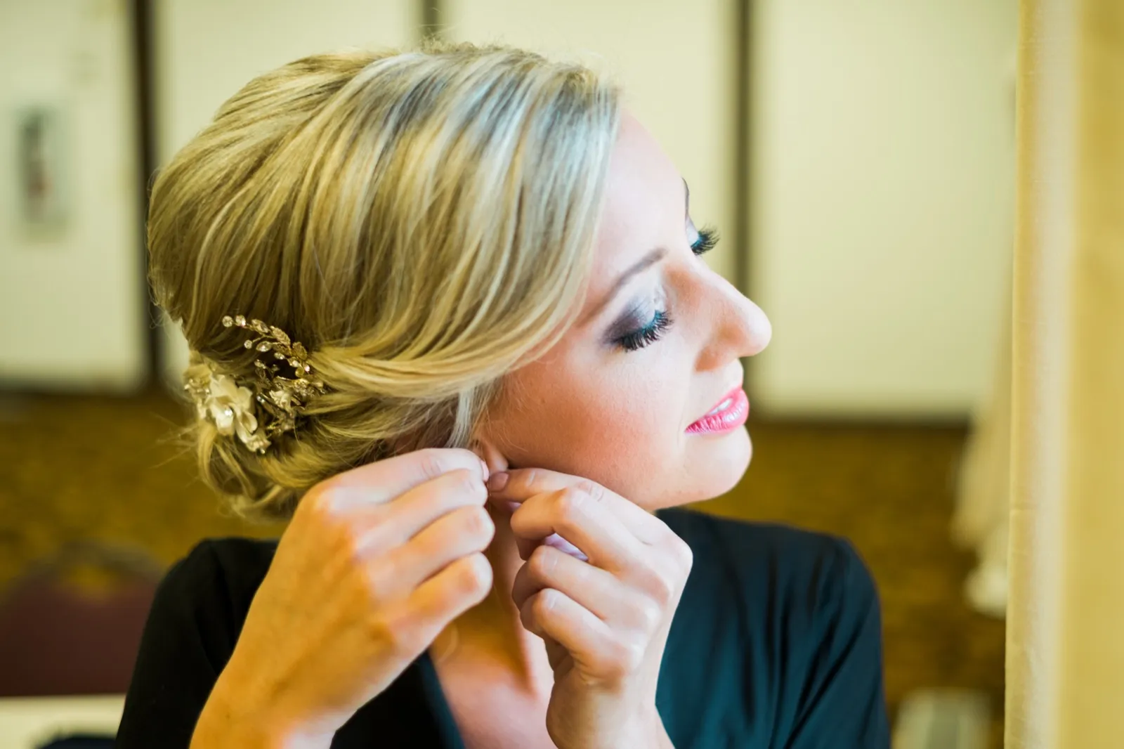 The bride in profile fastens an earring, her hair styled in a low updo with a floral hairpiece, lit by soft window light. — Tim Larsen Photography, Brainerd Lakes MN