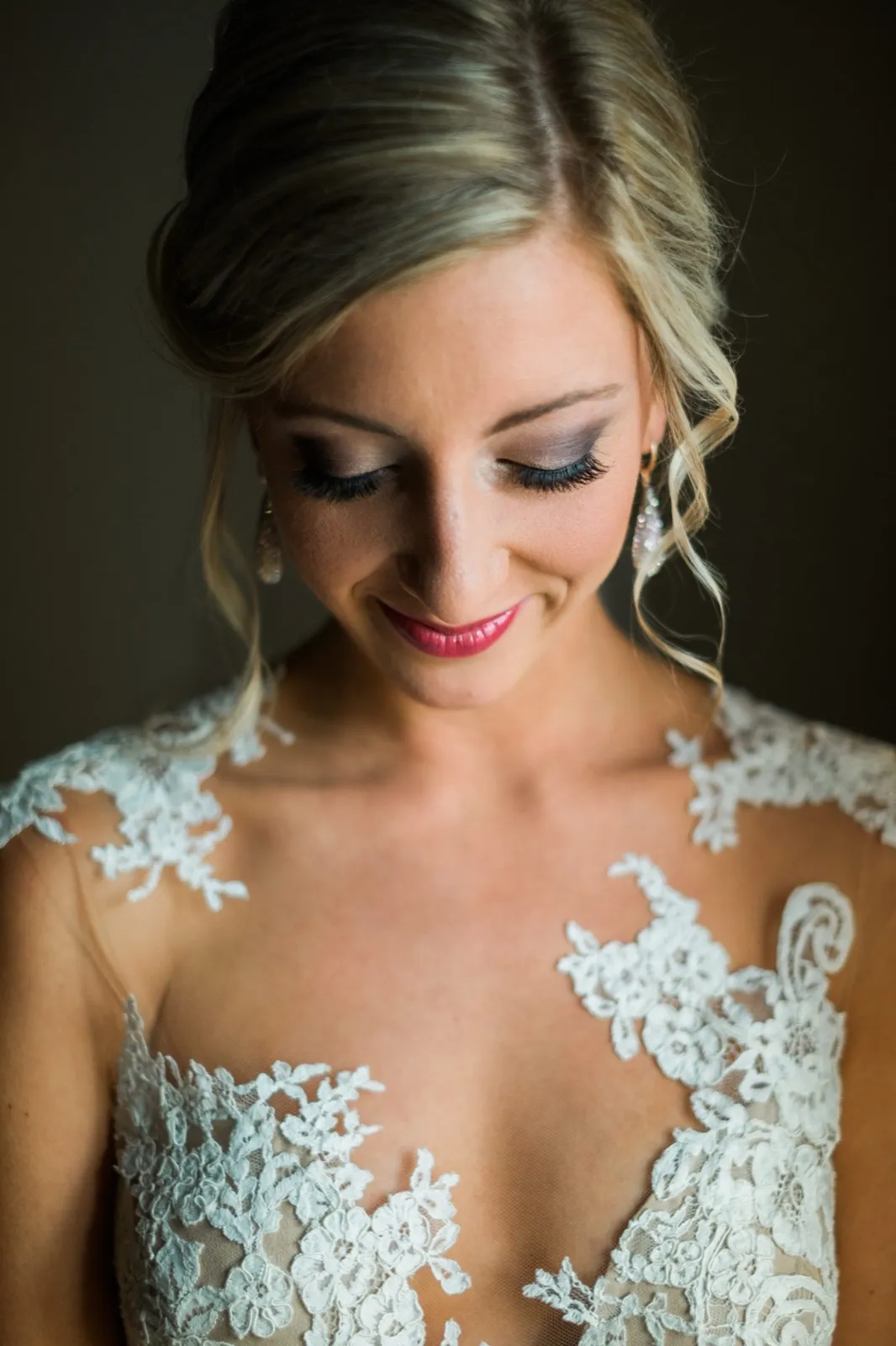 The bride looks downward with a soft smile in window light, her lace-detailed gown visible across her shoulders and chest. — Tim Larsen Photography, Brainerd Lakes MN