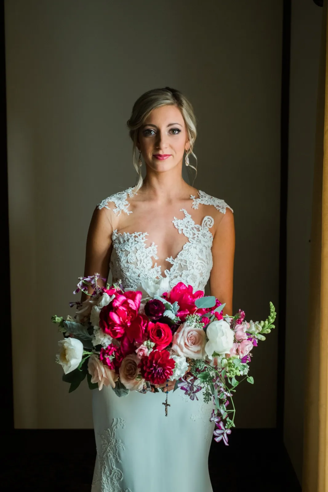 The bride holds a large bouquet of fuchsia and blush roses while standing in soft window light, wearing a lace bodice gown. — Tim Larsen Photography, Brainerd Lakes MN