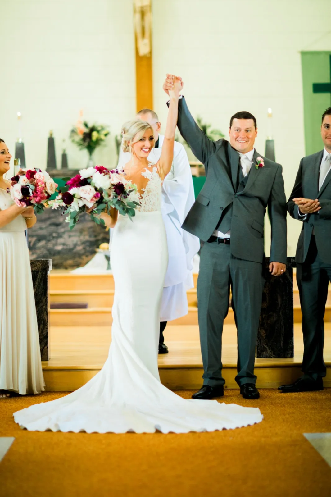 The bride and groom raise their joined hands in celebration at the altar as bridal party members clap beside them. — Tim Larsen Photography, Brainerd Lakes MN