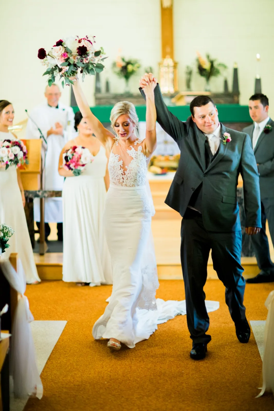 The bride and groom raise their joined hands and her bouquet overhead as they walk back down the church aisle just after the ceremony. — Tim Larsen Photography, Brainerd Lakes MN
