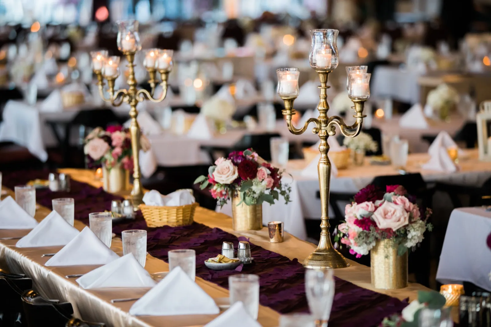 A long reception table set with gold candelabras, blush and burgundy floral centerpieces, and a deep plum runner extends into a candlelit ballroom at Cragun's Resort. — Tim Larsen Photography, Brainerd Lakes MN