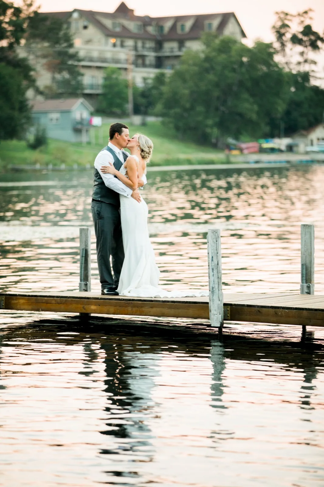 The bride and groom kiss on a wooden dock at dusk with Cragun's Resort and Gull Lake reflecting behind them. — Tim Larsen Photography, Brainerd Lakes MN