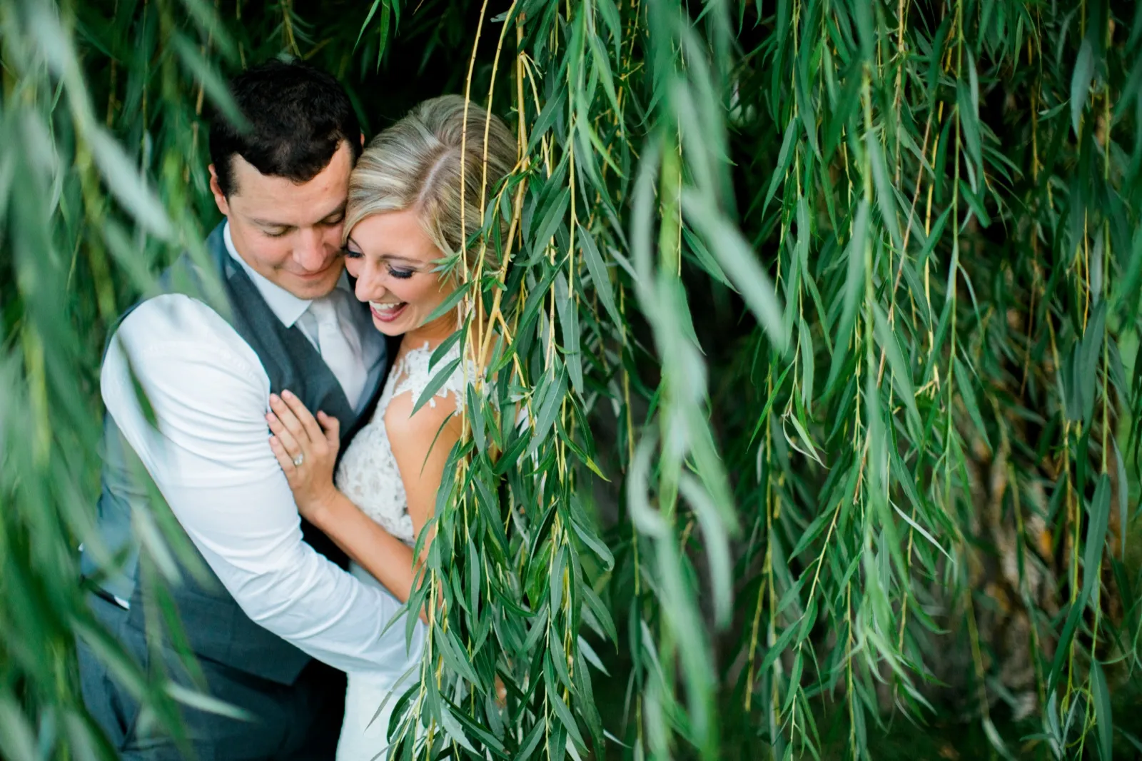 The bride laughs as the groom rests his forehead against hers, the couple framed by the hanging branches of a willow tree. — Tim Larsen Photography, Brainerd Lakes MN