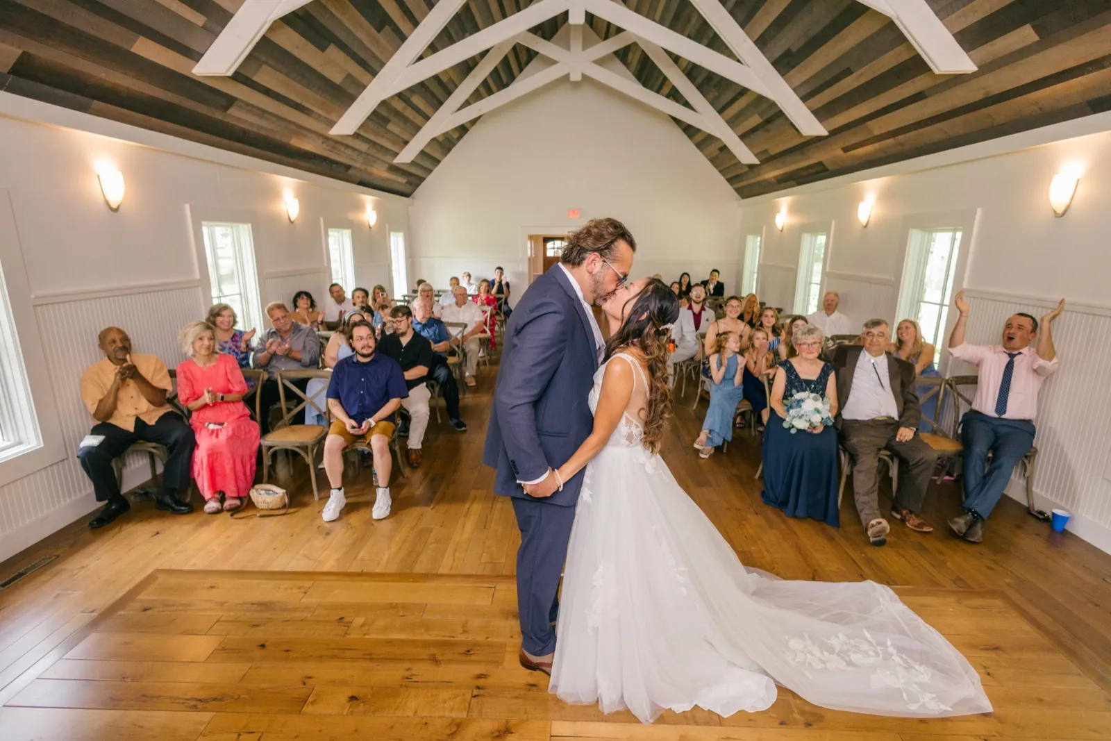 The couple kisses at the end of their ceremony in the wood-beamed Grand View Lodge chapel as guests on both sides clap and cheer — Tim Larsen Photography, Brainerd Lakes MN