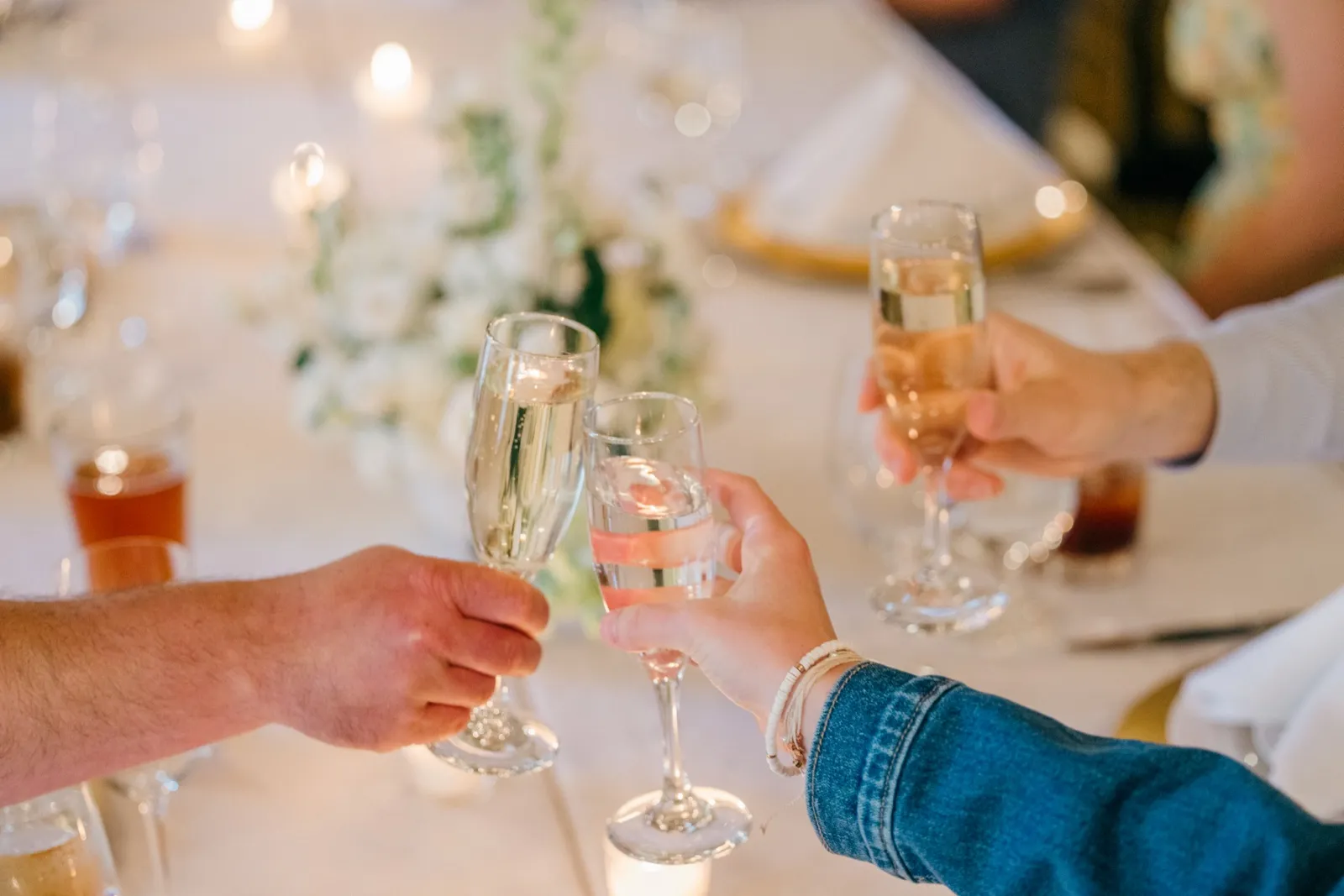 Three guests clink champagne flutes together over a candlelit reception table with white floral centerpieces — Tim Larsen Photography, Brainerd Lakes MN