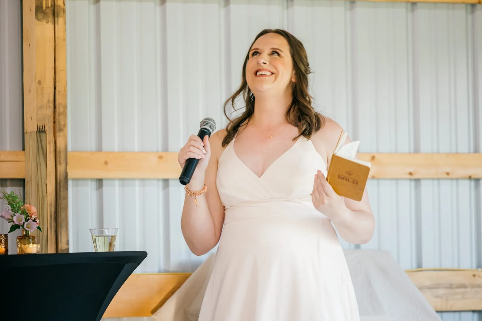 The bride laughs and looks upward while holding a microphone in one hand and a small notebook of speech notes in the other — Tim Larsen Photography, Brainerd Lakes MN