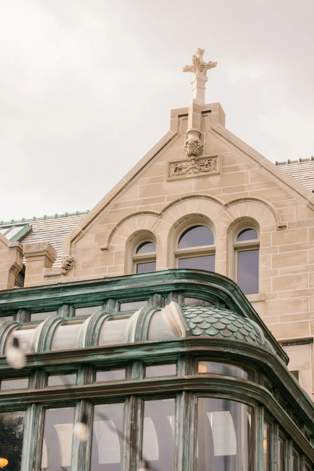 An upward view of the American Swedish Institute's stone gable topped with a carved cross, above a verdigris copper-and-glass conservatory. — Tim Larsen Photography, Minneapolis MN