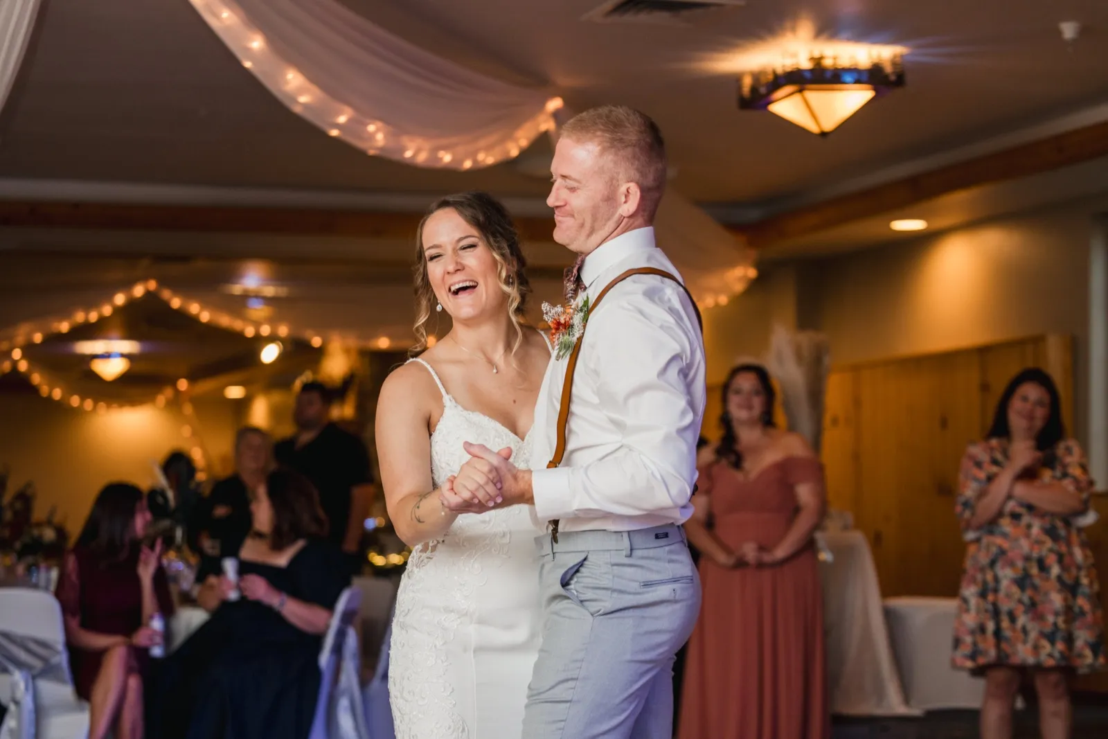 The bride laughs openly while dancing with the groom on a draped, string-lit dance floor as bridesmaids and guests watch from the edges — Tim Larsen Photography, Brainerd Lakes MN
