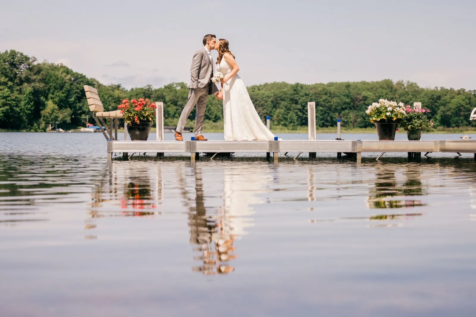 The bride and groom kiss on a dock surrounded by flower planters, their figures mirrored in the still lake water below. — Tim Larsen Photography, Brainerd Lakes MN