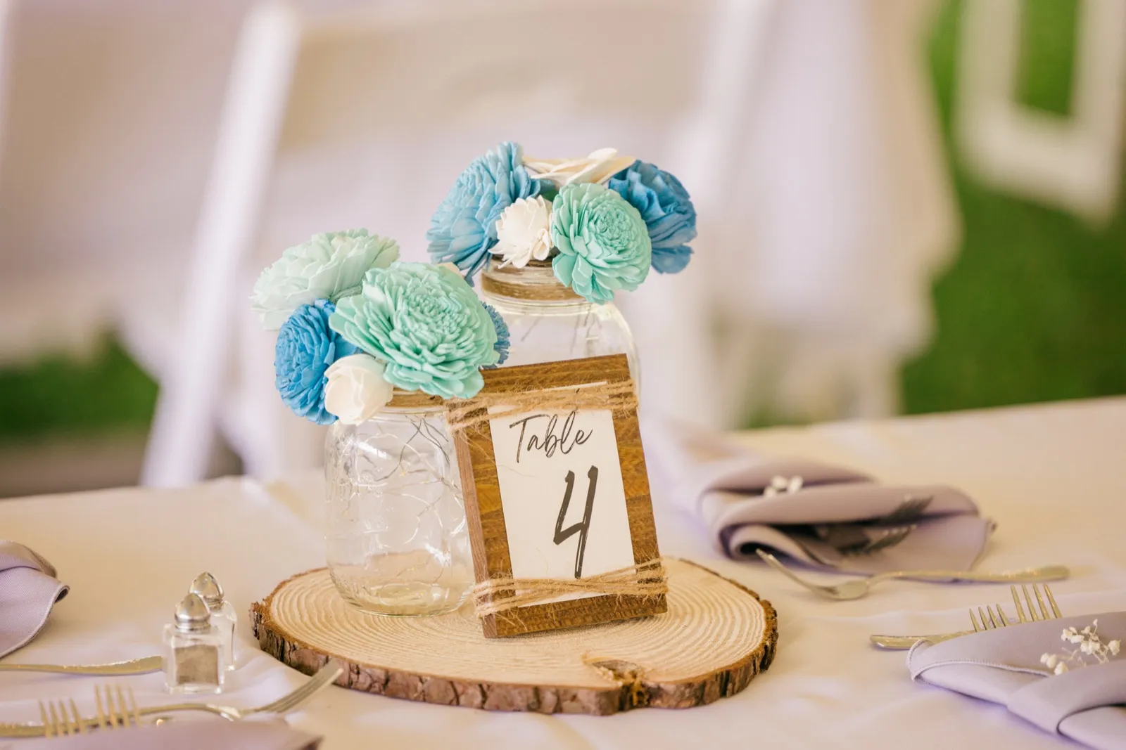 A mason jar centerpiece with blue and teal sola wood flowers sits on a wood slice next to a wooden Table 4 sign and lavender napkins. — Tim Larsen Photography, Brainerd Lakes MN