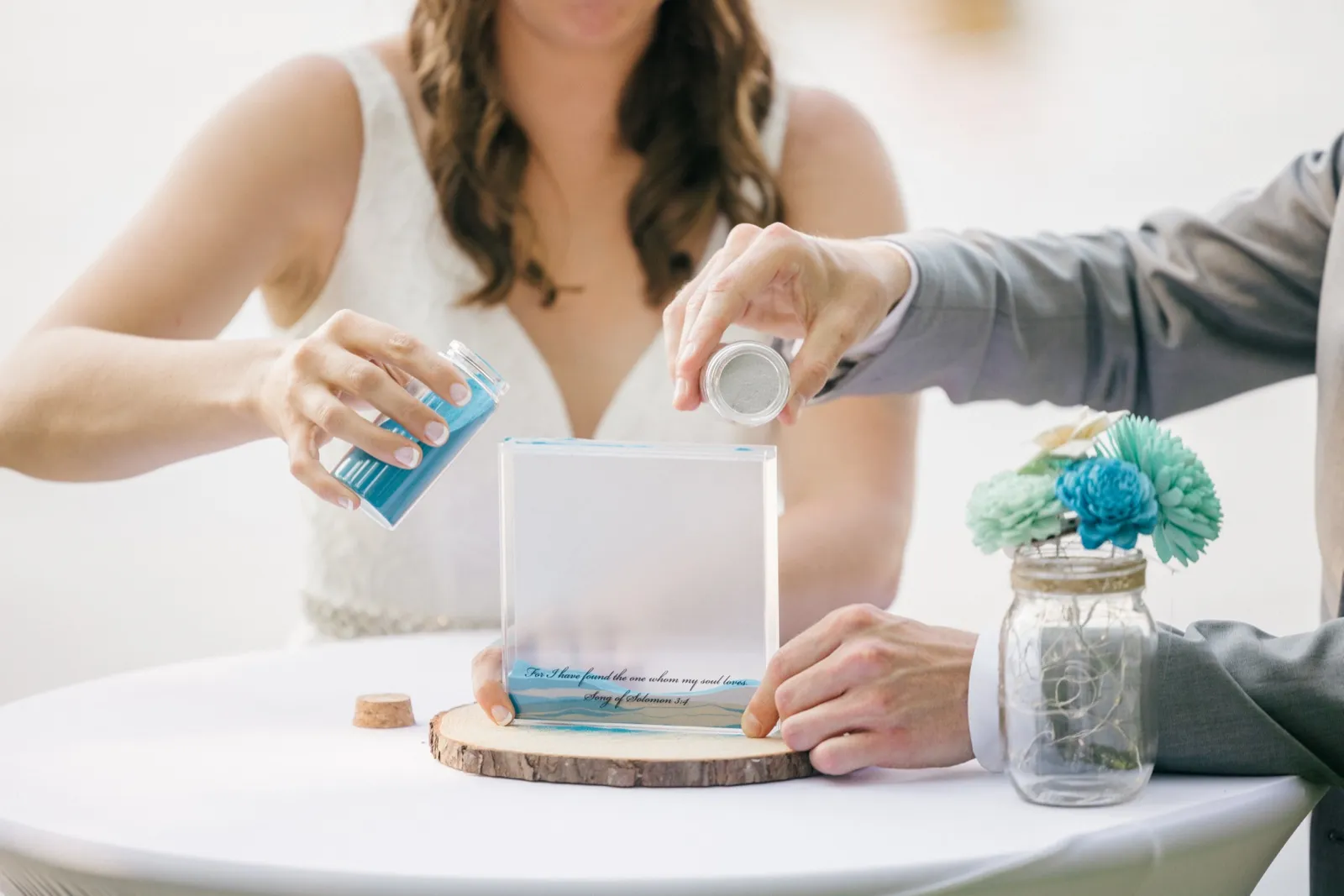 The bride and groom pour blue sand into an engraved glass vessel inscribed with Song of Solomon 3:4 during a unity ceremony. — Tim Larsen Photography, Brainerd Lakes MN