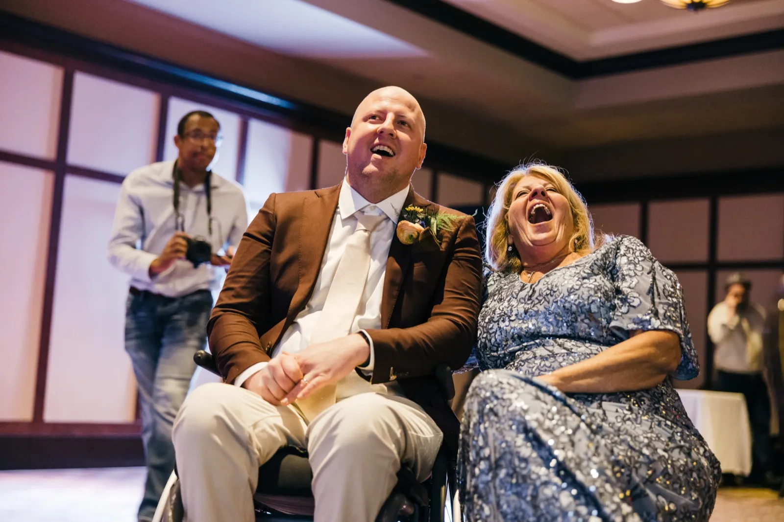 The groom and his mother throw their heads back laughing together during a parent dance at the reception, with a second photographer visible in the background. — Tim Larsen Photography, Brainerd Lakes MN