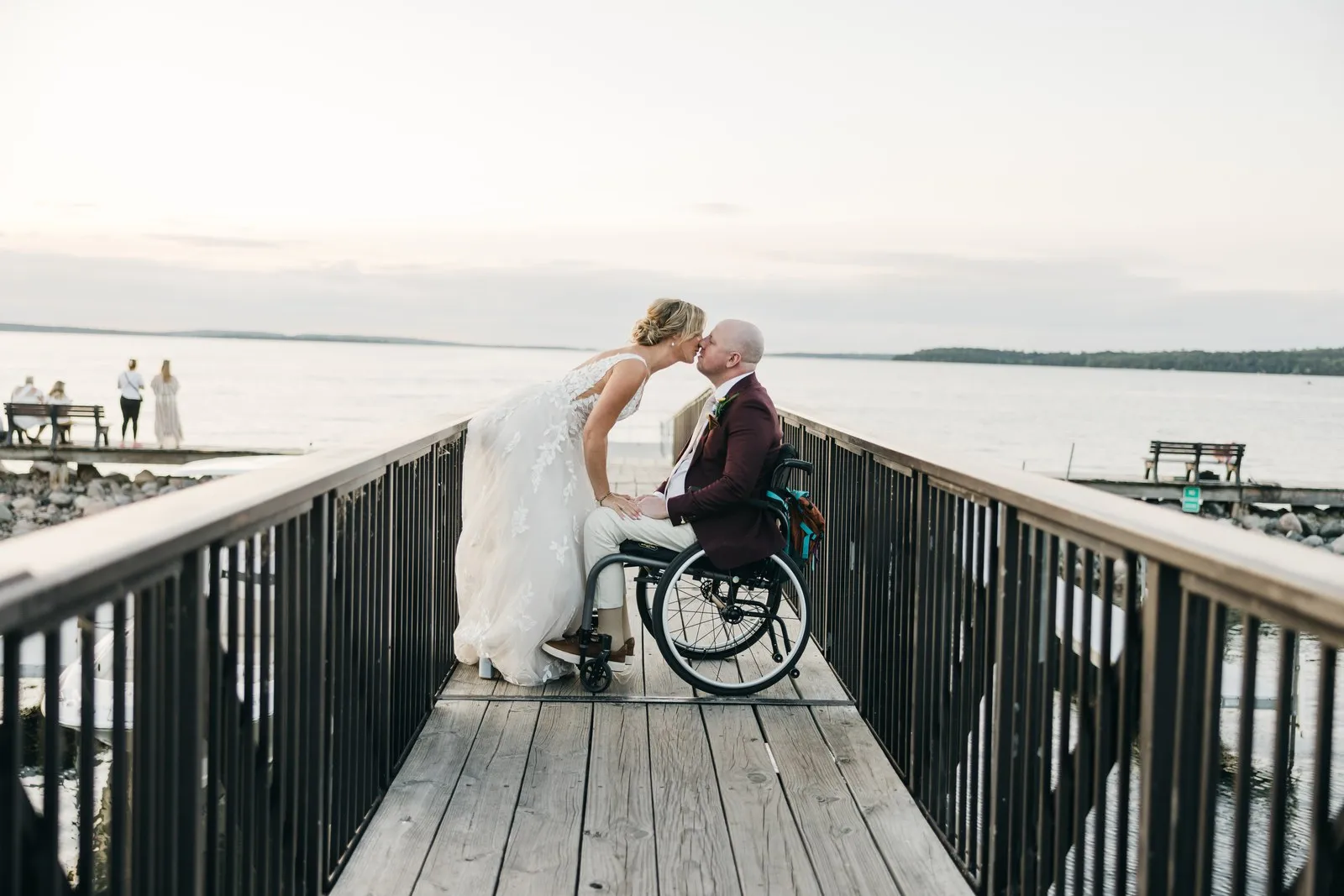 Jenna leans in to kiss Joe at the center of the marina dock at dusk, the railings drawing symmetrical lines out toward pale water on Leech Lake. — Tim Larsen Photography, Brainerd Lakes MN