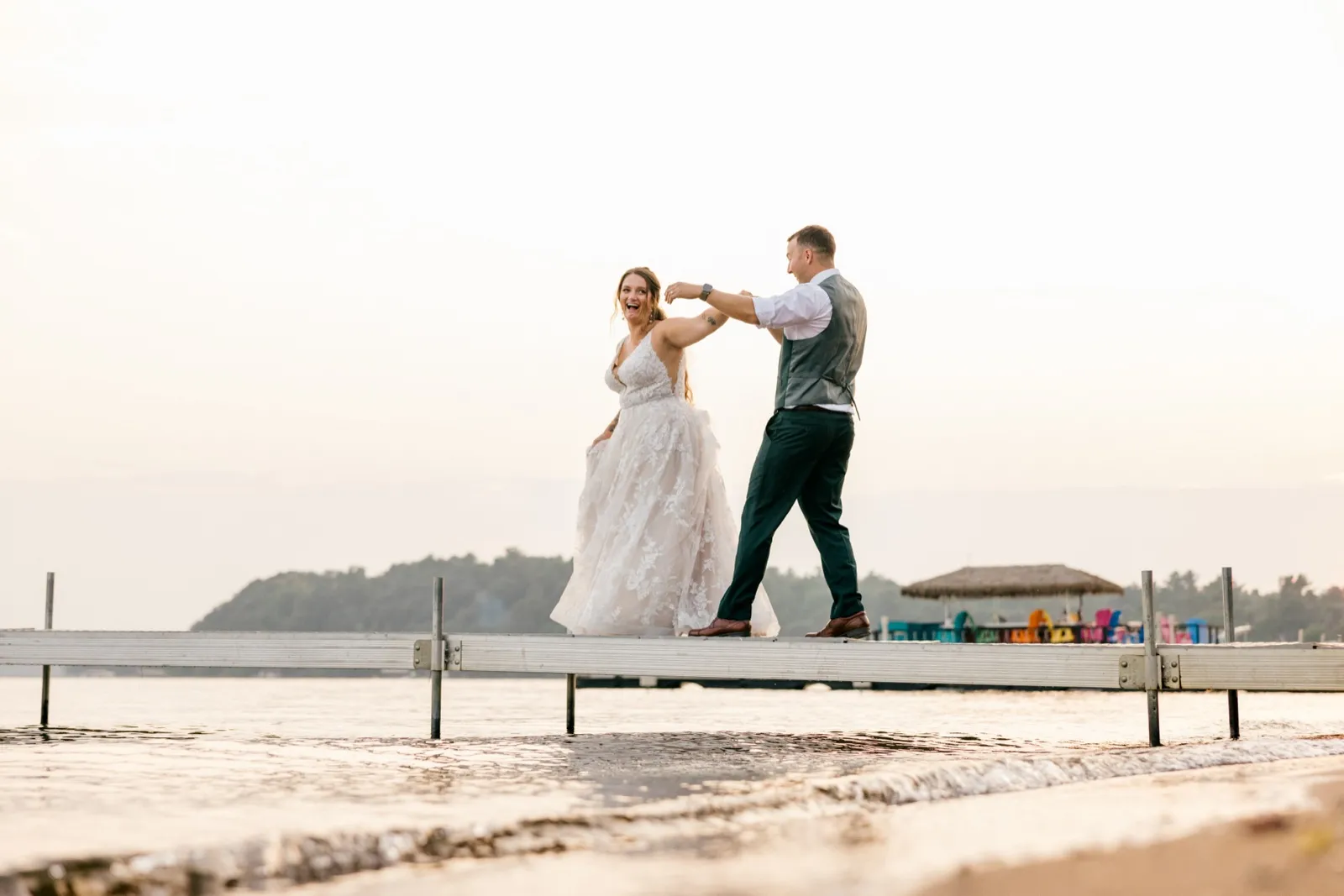 Eric twirls Chelsea on a long wooden dock at golden hour as she laughs, with Gull Lake and the resort beach behind them — Tim Larsen Photography, Brainerd Lakes MN