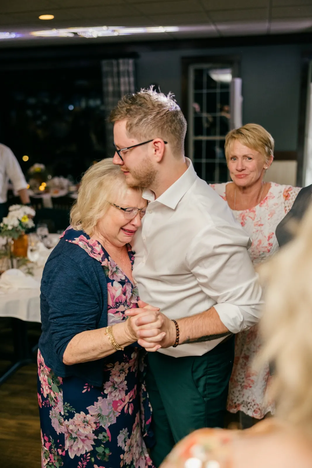 Eric holds his tearful mother during their dance while another woman watches with an empathetic expression behind them — Tim Larsen Photography, Brainerd Lakes MN