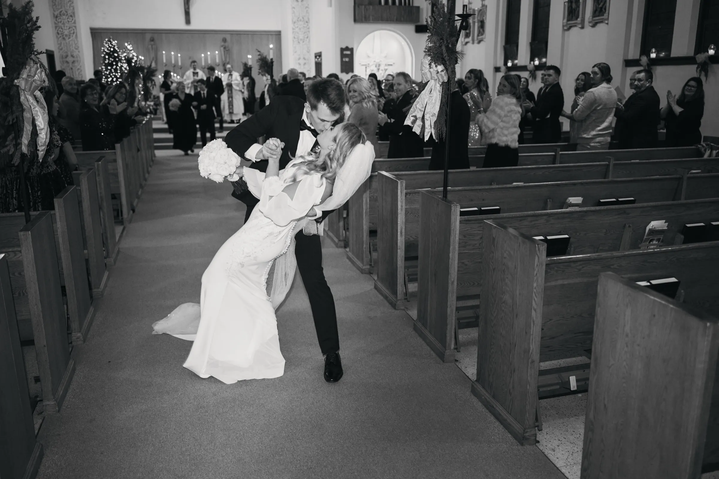 Sam dips Madeline into a kiss in the center of the church aisle as guests in the pews applaud around them — Tim Larsen Photography, Brainerd Lakes MN
