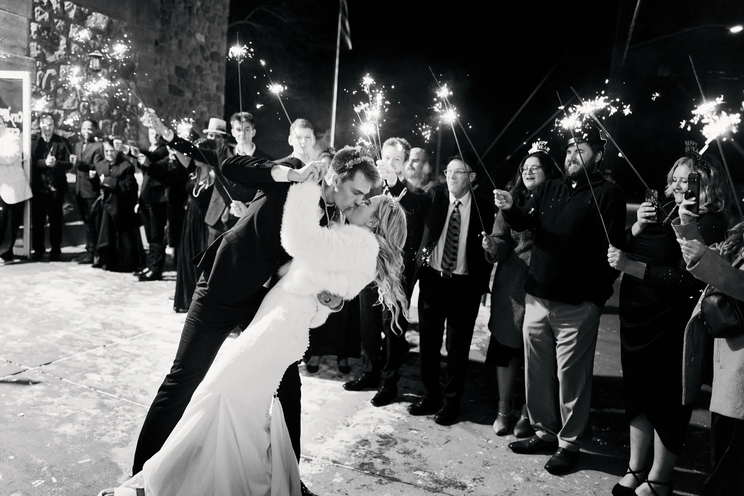 Sam dips Madeline for a kiss inside a sparkler tunnel formed by guests at night, a stone wall behind them — Tim Larsen Photography, Brainerd Lakes MN