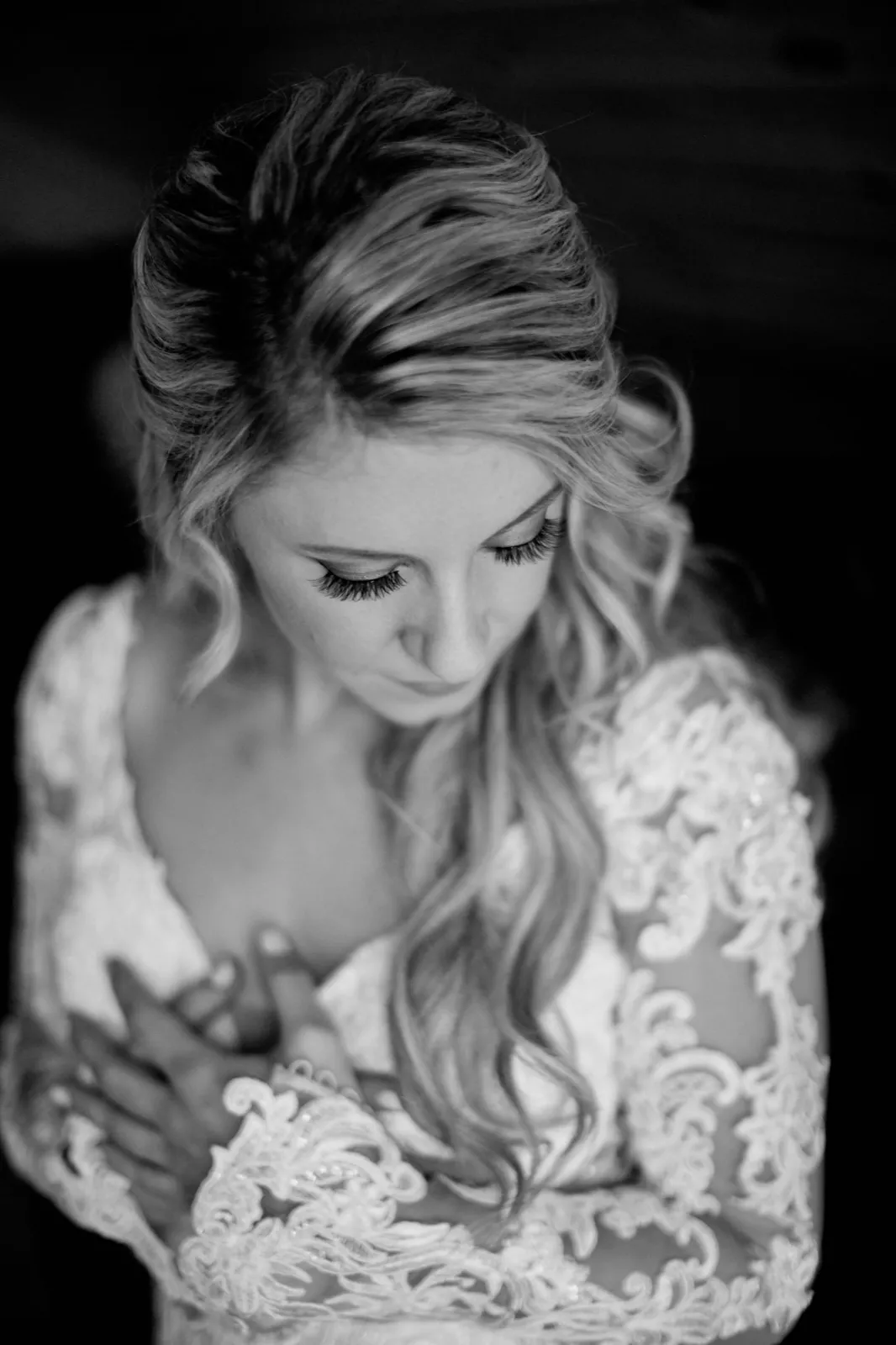Black-and-white frame of the bride looking down with her hands clasped at her chest, lace sleeves across her arms — Tim Larsen Photography, Brainerd Lakes MN