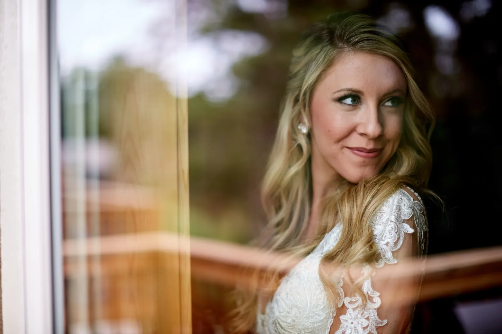 The bride looks to the side behind a window, warm wood reflections streaking the glass across her lace gown — Tim Larsen Photography, Brainerd Lakes MN