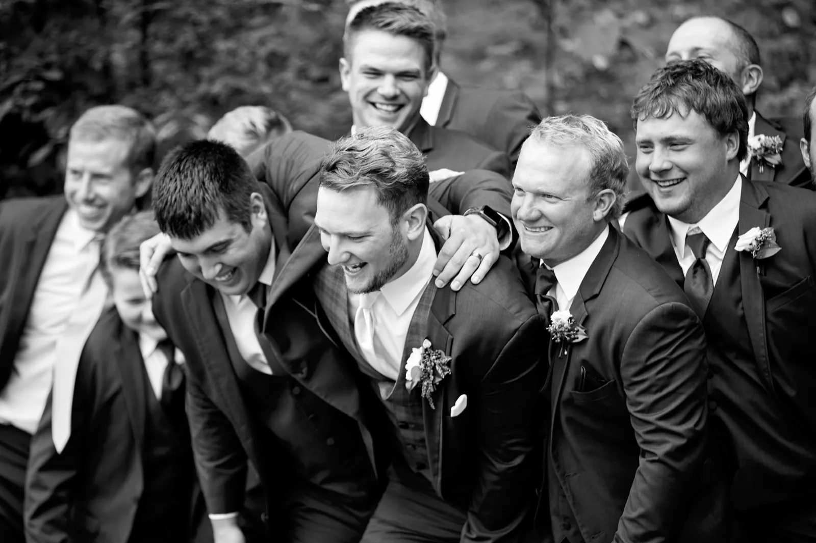 Black-and-white frame of the groom laughing as his groomsmen crowd in close around him — Tim Larsen Photography, Brainerd Lakes MN