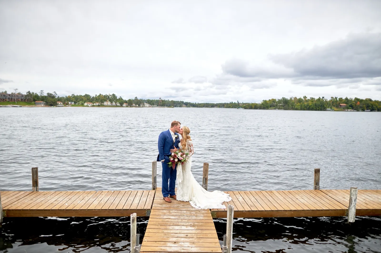 The bride and groom kiss at the end of a T-shaped dock reaching into Gull Lake under a wide cloudy sky at Cragun's Resort — Tim Larsen Photography, Brainerd Lakes MN