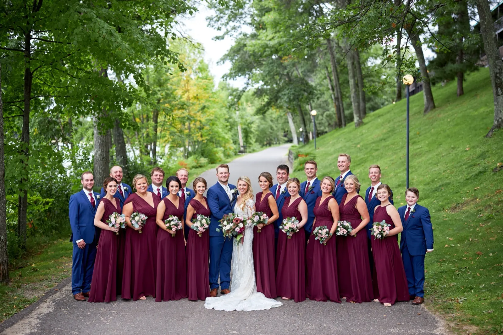 The bride and groom centered in their bridal party — burgundy dresses, navy suits — on a tree-lined path at Cragun's Resort — Tim Larsen Photography, Brainerd Lakes MN