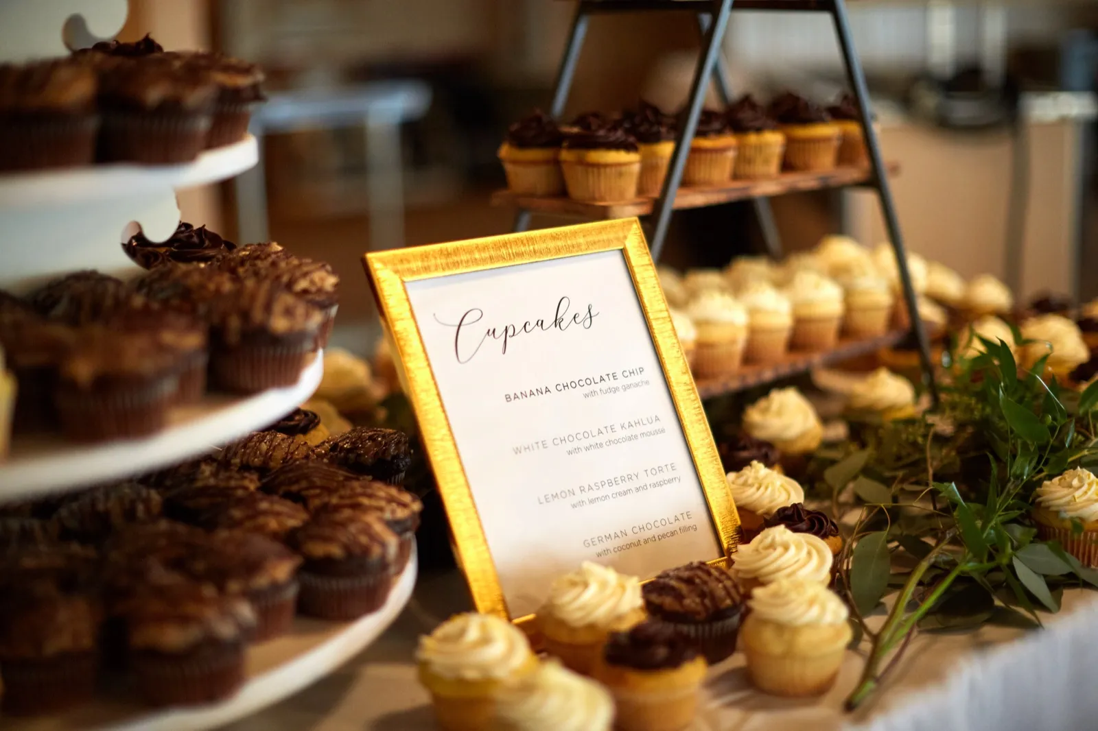 A gold-framed handwritten menu among tiered displays of chocolate and vanilla cupcakes with greenery — Tim Larsen Photography, Brainerd Lakes MN