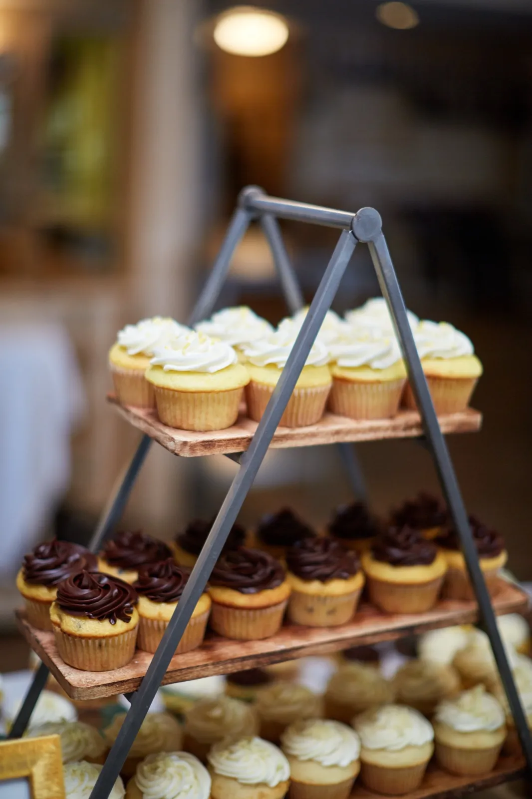 A tiered metal-and-wood A-frame stand of vanilla and chocolate cupcakes at the reception dessert table — Tim Larsen Photography, Brainerd Lakes MN