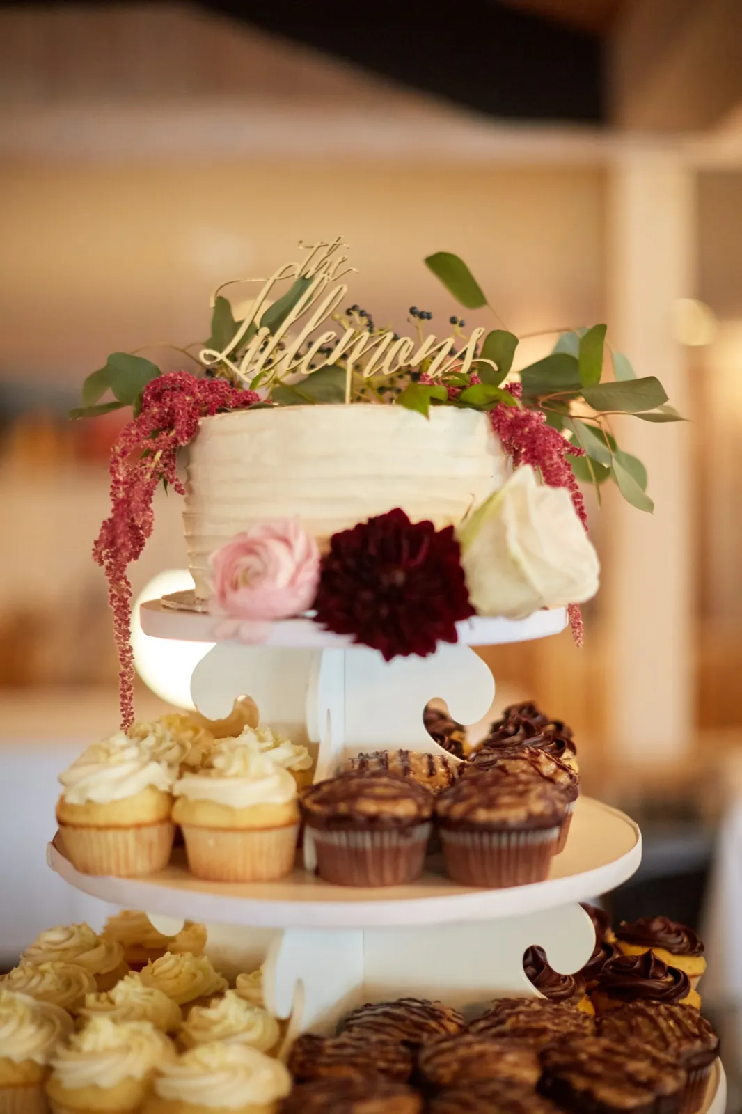 A single-tier white cake with a gold script topper and burgundy and blush florals above an array of cupcakes — Tim Larsen Photography, Brainerd Lakes MN