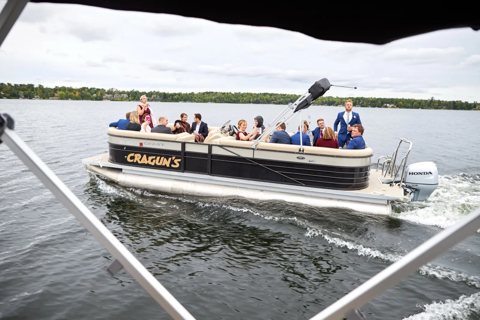 The wedding party rides a Cragun's-branded pontoon across Gull Lake under overcast skies — Tim Larsen Photography, Brainerd Lakes MN