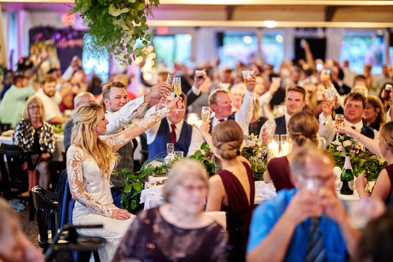 The bride and groom raise champagne glasses at the head table as the full room mirrors the toast behind them — Tim Larsen Photography, Brainerd Lakes MN
