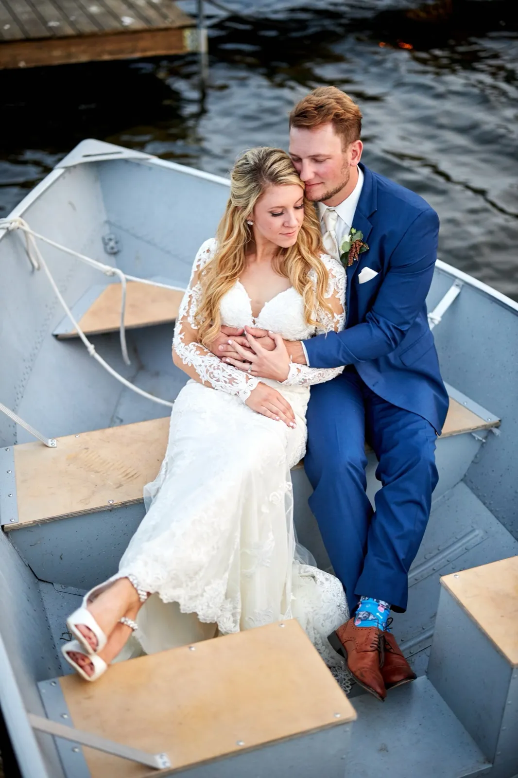 The bride and groom sit close in an aluminum boat on the lake, the groom resting his face against her hair — Tim Larsen Photography, Brainerd Lakes MN
