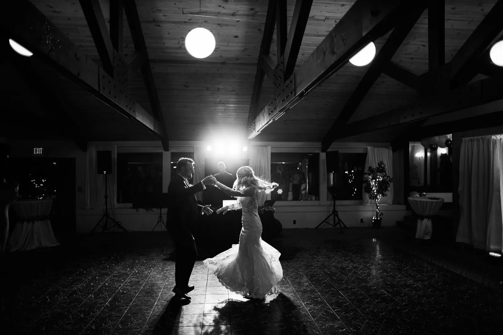The bride spins in her gown as the groom guides her hand, silhouetted by stage light under the wood-truss ceiling — Tim Larsen Photography, Brainerd Lakes MN