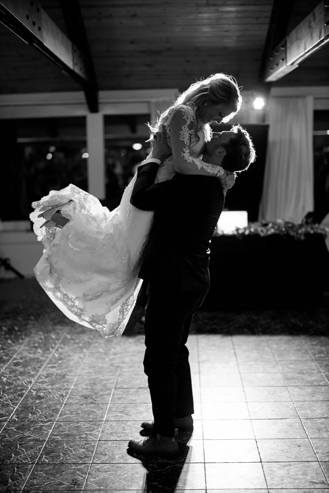 The groom lifts the bride above his head on the dance floor, backlight rimming them both (black and white) — Tim Larsen Photography, Brainerd Lakes MN