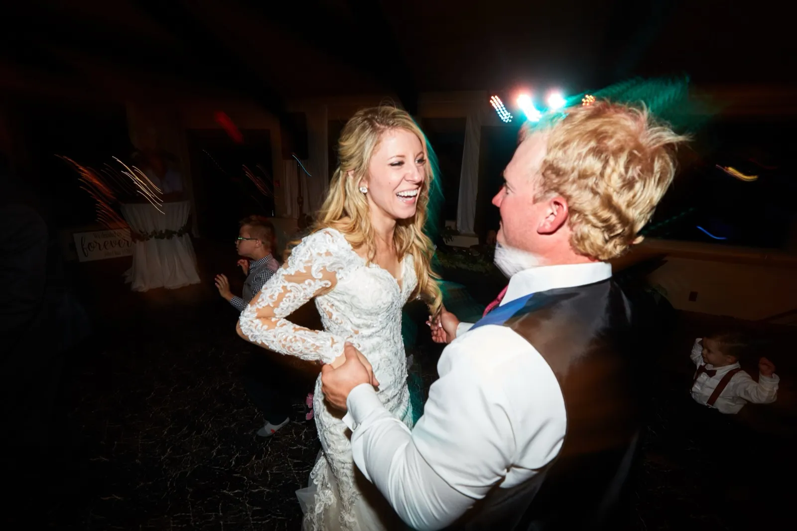 The bride laughs wide-open dancing with the groom, colored stage light streaking behind them — Tim Larsen Photography, Brainerd Lakes MN