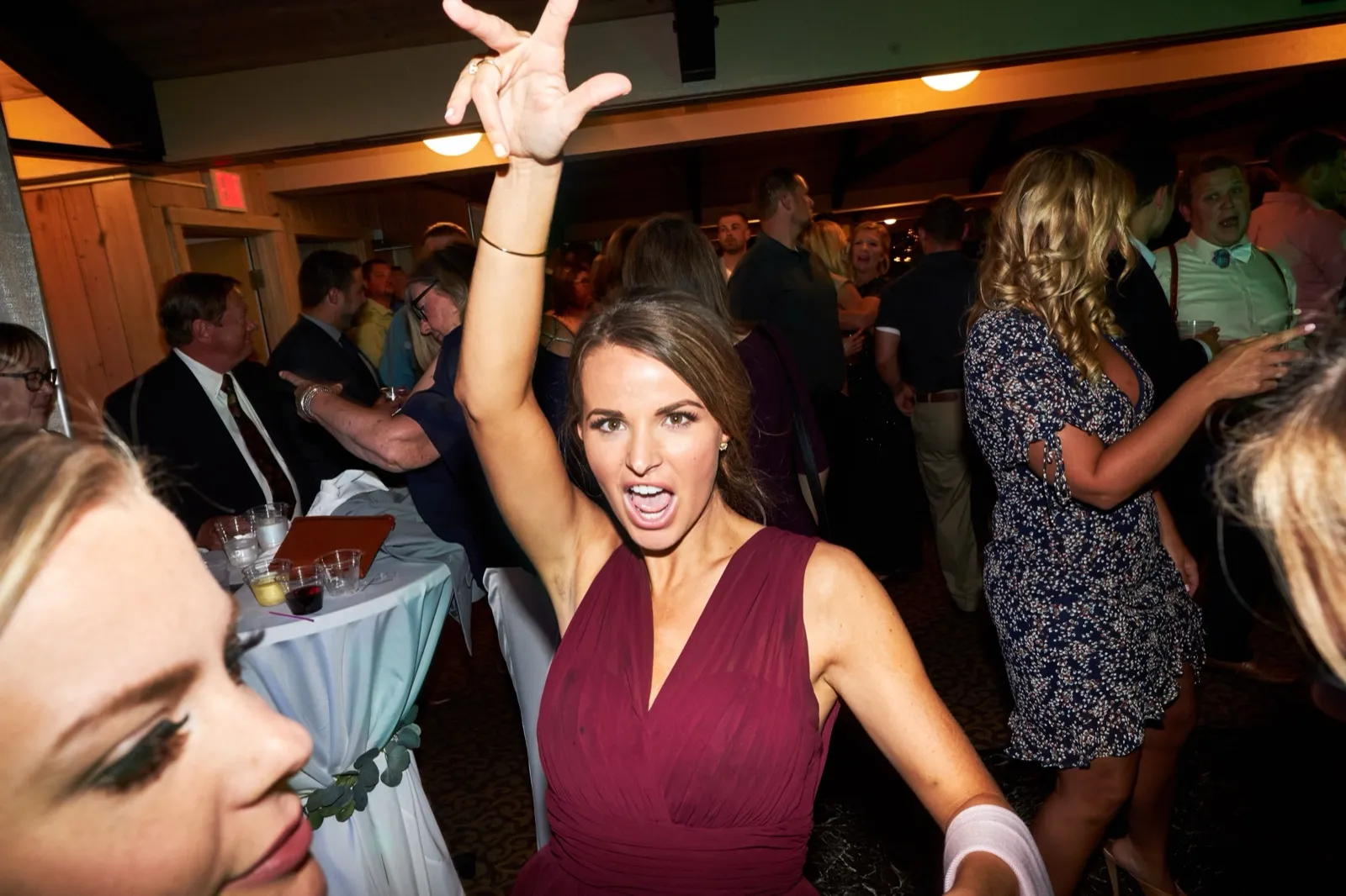 A bridesmaid in burgundy throws an arm overhead and shouts mid-cheer on the crowded dance floor — Tim Larsen Photography, Brainerd Lakes MN