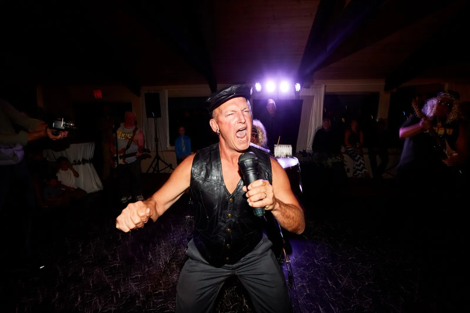The cover band's lead singer in a leather vest belts into the mic under purple stage light — Tim Larsen Photography, Brainerd Lakes MN