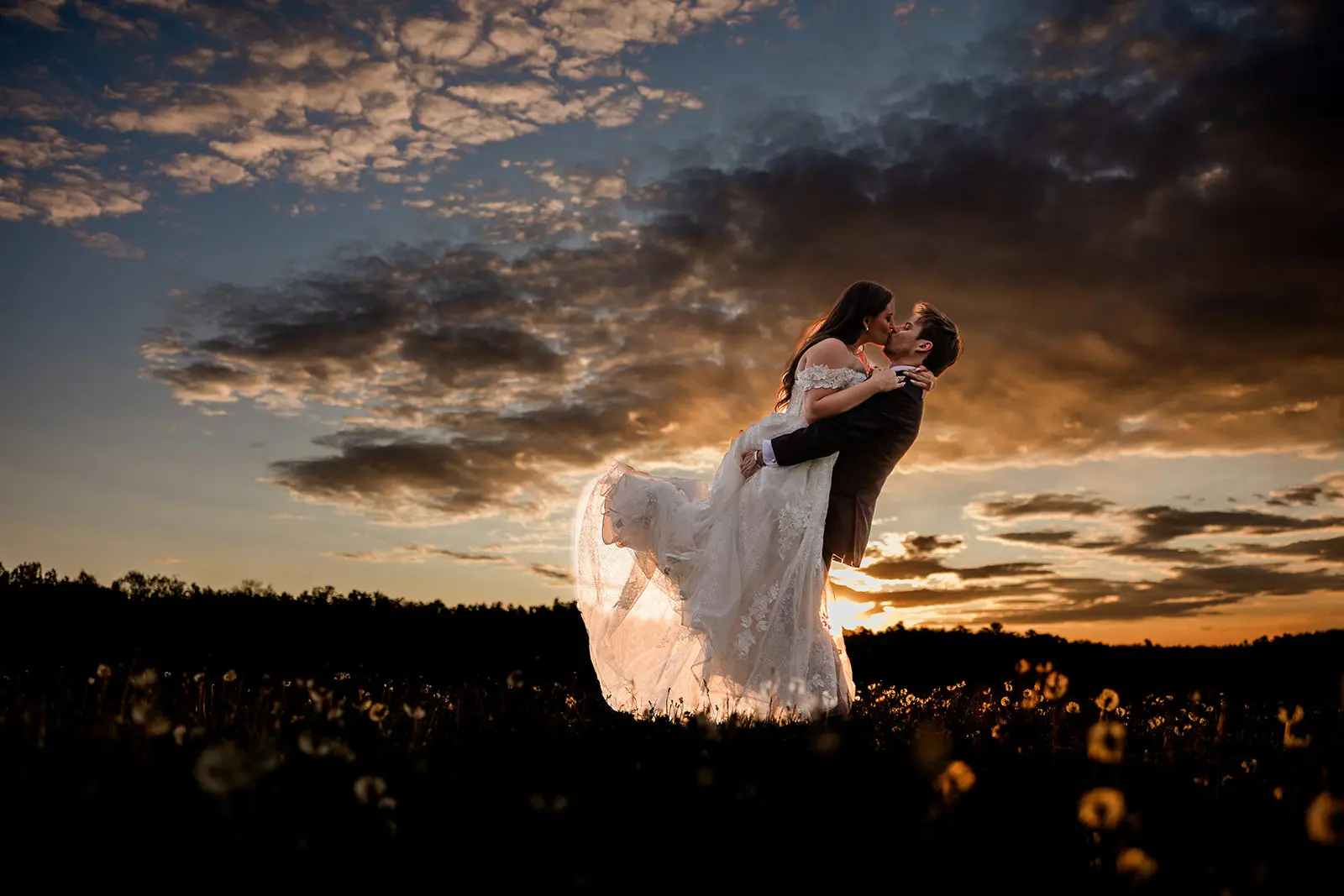 Sunset dip kiss in a wildflower field beneath a banded pastel sky — Tim Larsen Photography, Brainerd Lakes MN