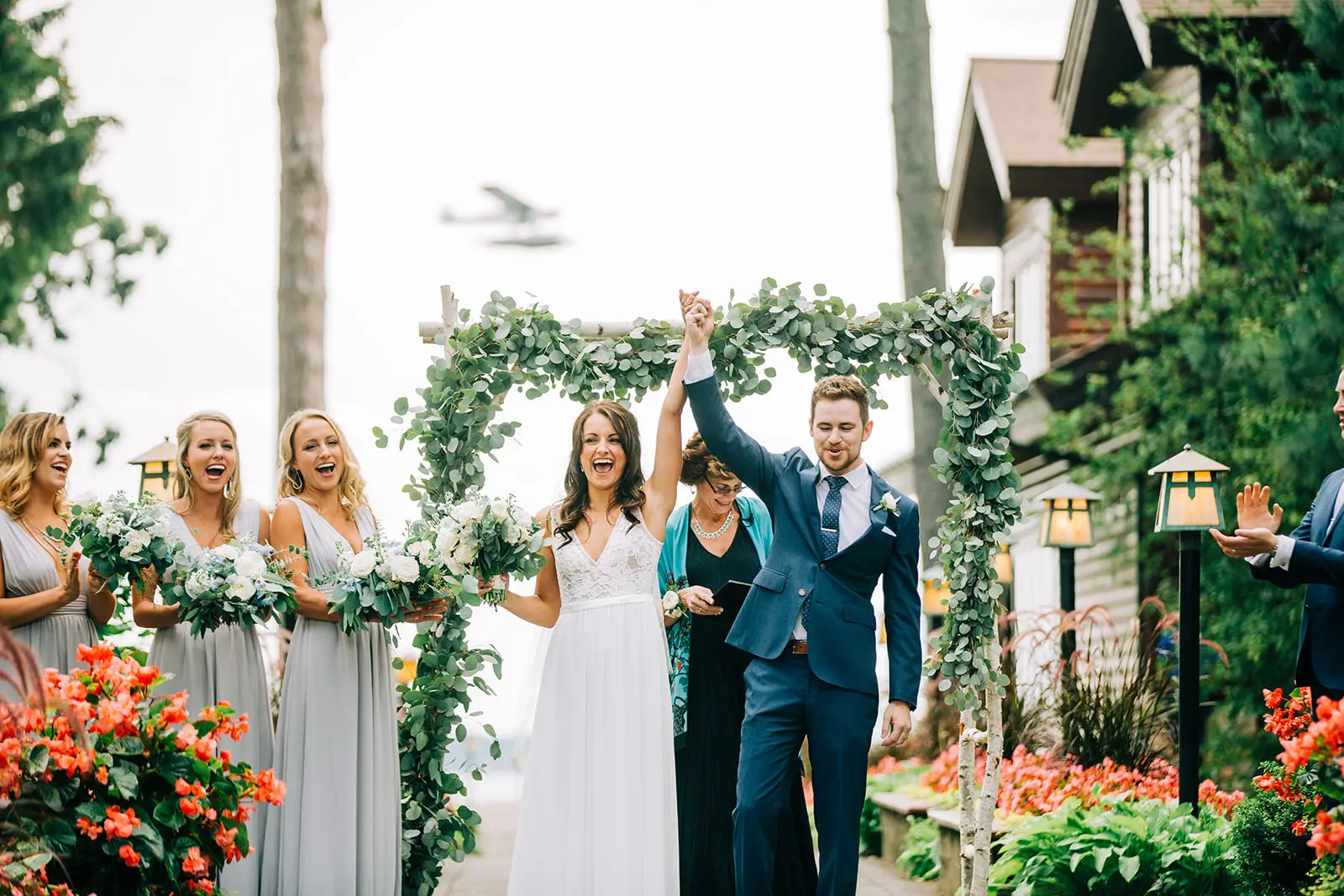 Wedding party erupting in cheer beneath a eucalyptus-covered arch at the ceremony recessional — Tim Larsen Photography, Brainerd Lakes MN