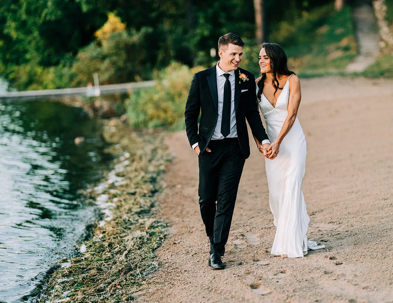 Couple walking hand-in-hand along a lakeside beach at golden hour — Tim Larsen Photography, Brainerd Lakes MN