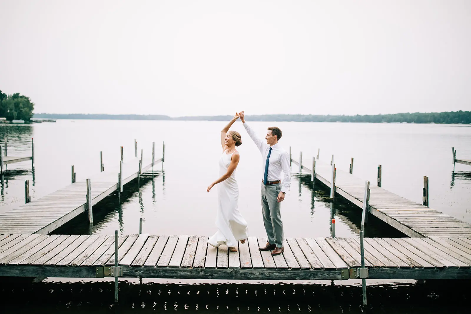 Couple twirling on a wooden dock as the lake stretches behind them — Tim Larsen Photography, Brainerd Lakes MN
