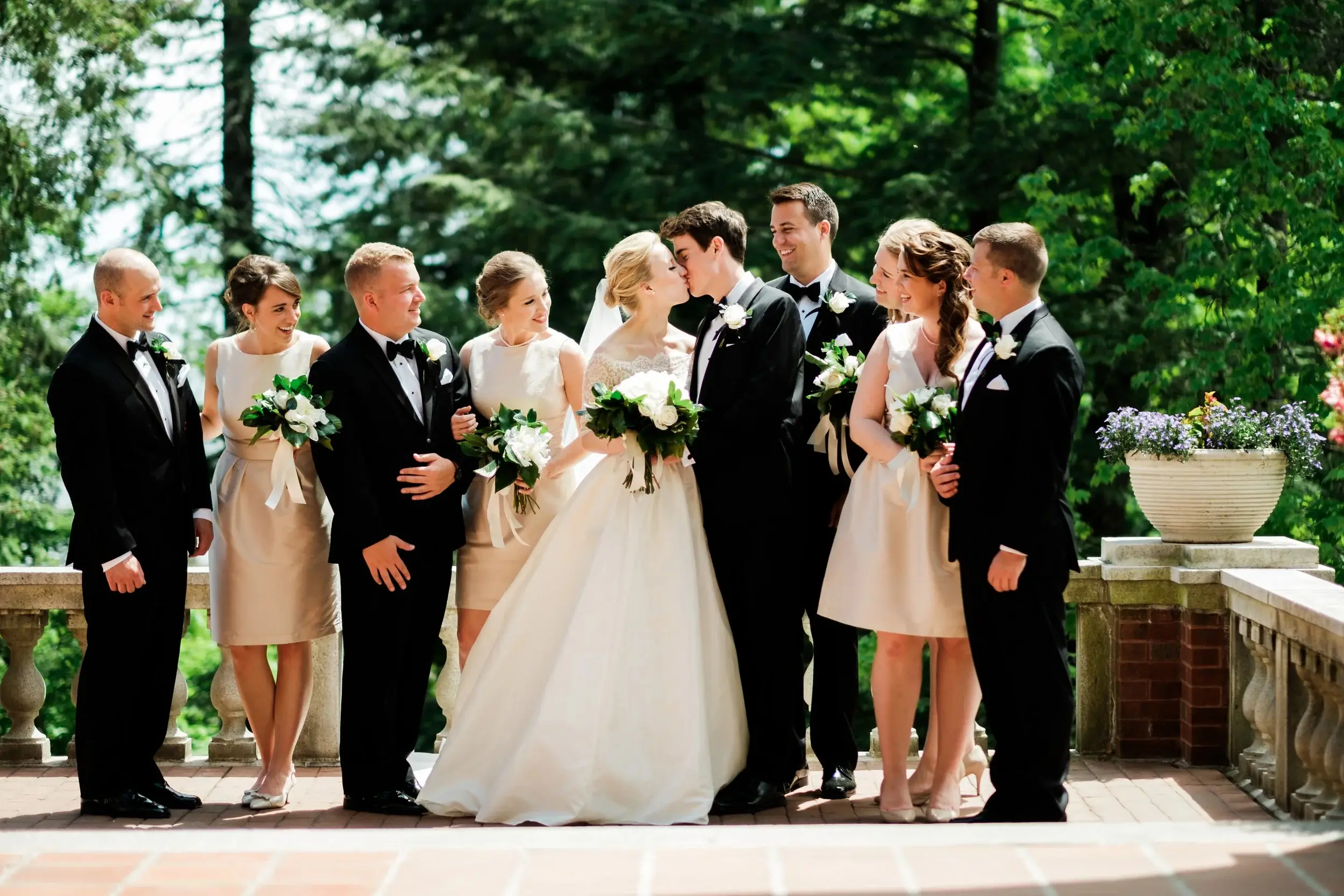 Classic wedding party portrait on a stone-balustrade terrace, the couple kissing center — Tim Larsen Photography, Brainerd Lakes MN