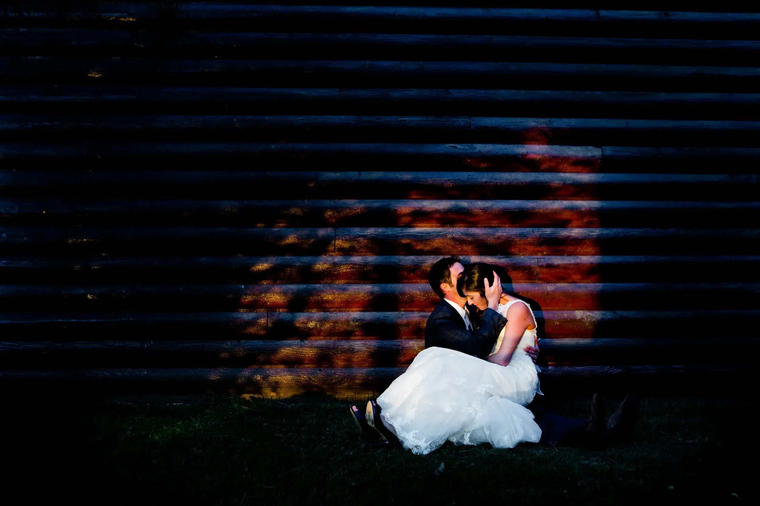 Couple seated against a barn wall at night, red stained-glass light pooling across the wood slats — Tim Larsen Photography, Brainerd Lakes MN