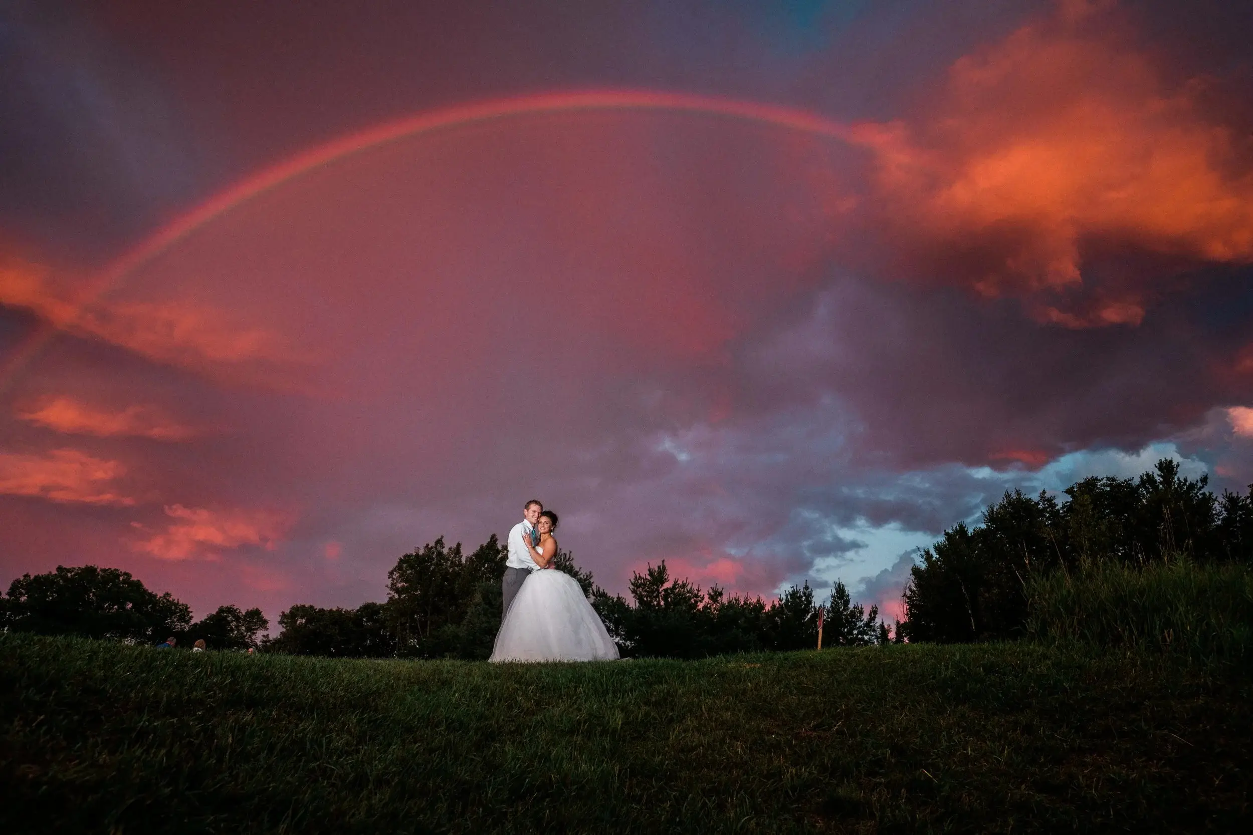 Bride and groom beneath a rainbow and a burning pink sunset after a storm — Tim Larsen Photography, Brainerd Lakes MN