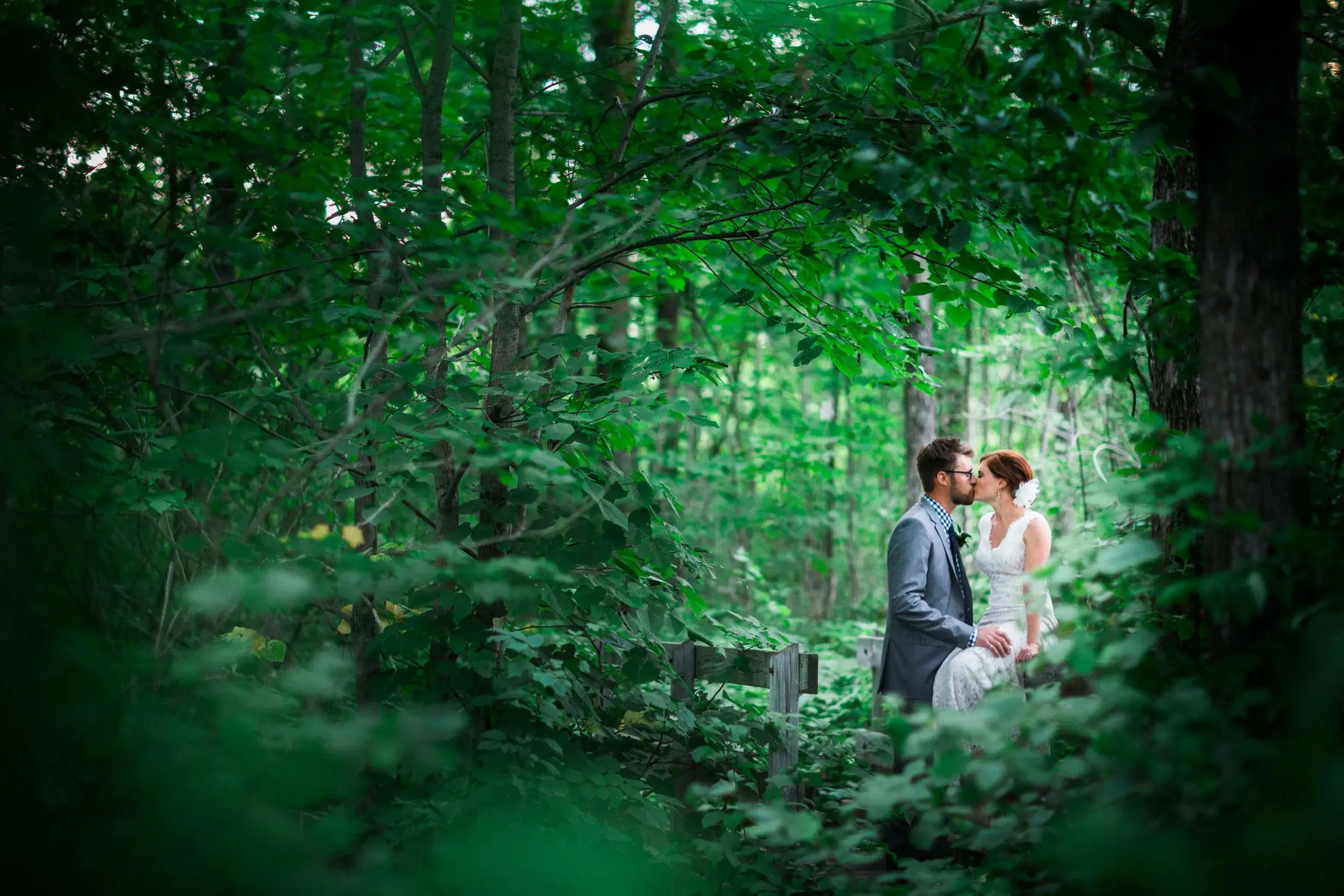 Couple kissing framed by dappled green forest leaves — Tim Larsen Photography, Brainerd Lakes MN